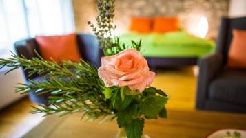 A rose in a vase on a table in a room with a green couch and orange cushions in the background.