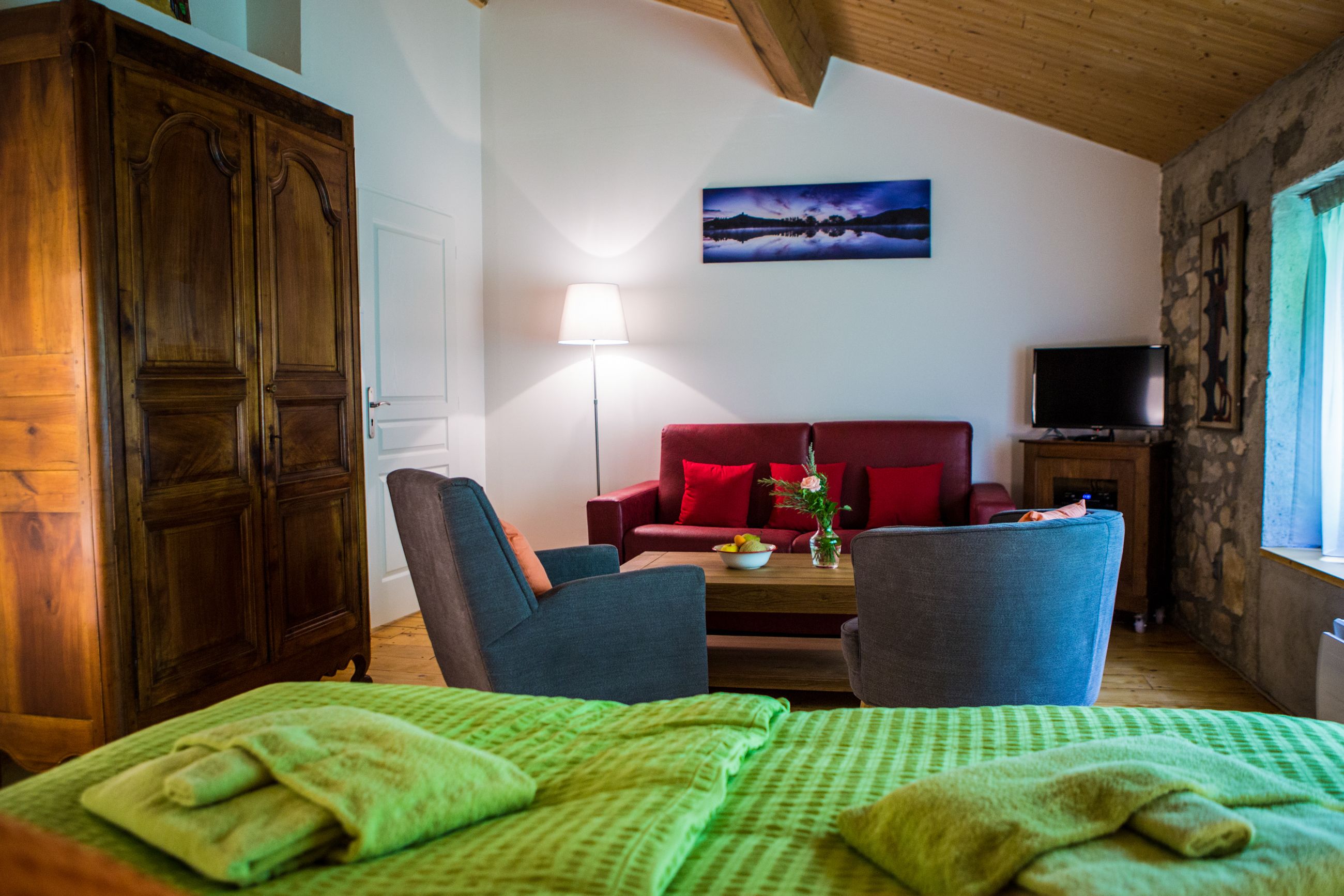 A room with a bed, two armchairs, a sofa, a lamp, a TV, and a painting on the wall.
