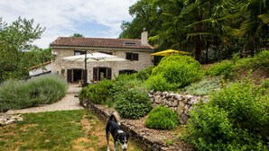 A stone house with a tiled roof, surrounded by lush greenery and a stone wall. - Moulin d'Entre Les Roches (Puivert)