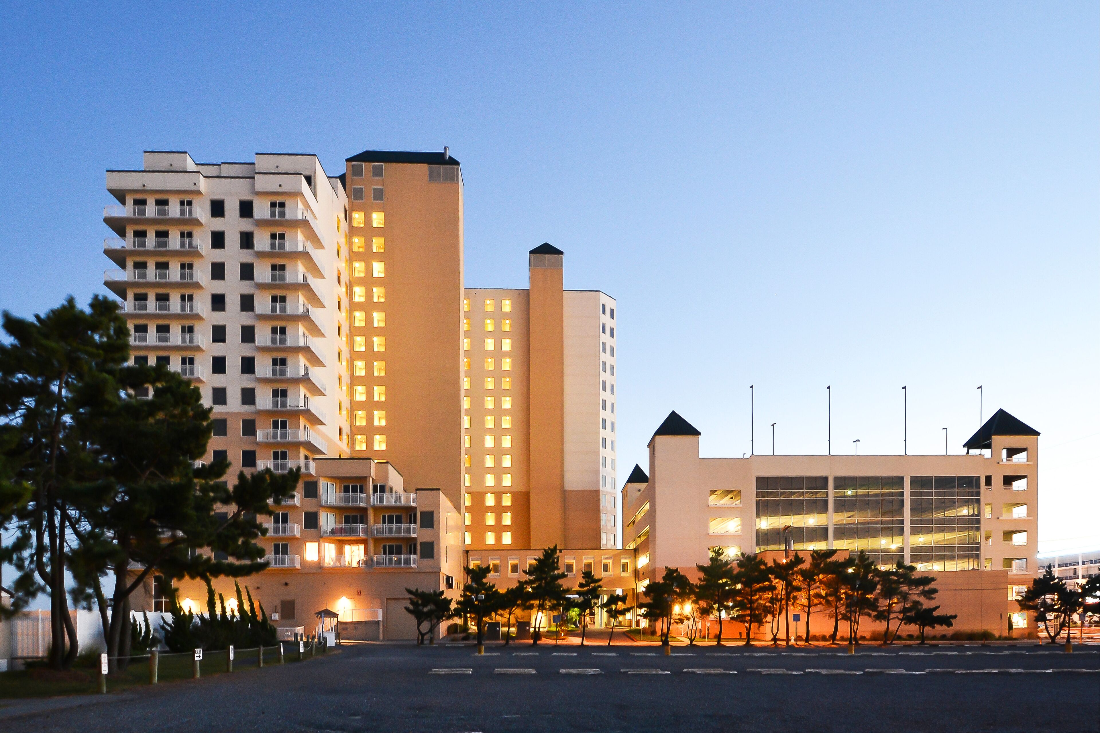 A multi-story hotel with balconies, a parking lot, and a building with a glass facade.