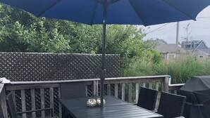 En terrasse med et bord og stole, en blå parasol og et espalierhegn.