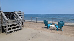 Una terraza de madera con una escalera que lleva a una zona de playa, con dos sillas azules y una mesita.