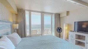 Ein Hotelzimmer mit einem großen Bett, einem Fernseher, einem Ventilator und Meerblick.