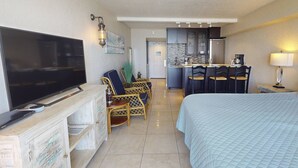 Ein Hotelzimmer mit Fernseher, einem Bett, einer Essecke mit Stühlen, einer Küche und einer Lampe.
