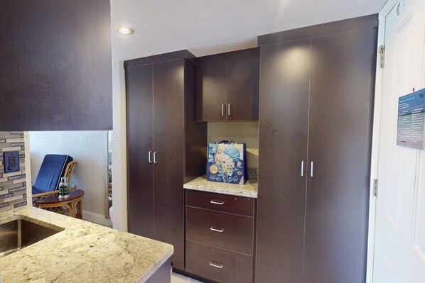 A modern kitchen with dark cabinets, a granite countertop, and a wicker chair. - Amazing Beachfront Studio w/Private Balcony! Beachside Pool, Tiki Bar, Sand Volleyball, Fishing Dock (Treasure Island)
