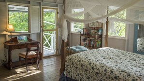 Un dormitorio con cama con dosel, un escritorio con una computadora portátil, una estantería y una silla de mimbre.