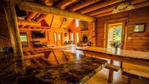 Ein Blockhaus-Interieur mit Kamin aus Stein, einem Holzespeisesaal und einem an der Wand montierten Fernseher.