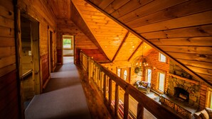Ein Holzinnenraum mit schrägverdeckter Decke, einem Steinkamin und Blick durch ein Fenster.
