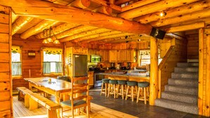 Ein Blockhaus-Interieur mit einem Holzespeisesaal, Barhocker, einer Küchenzeile und einer Treppe.