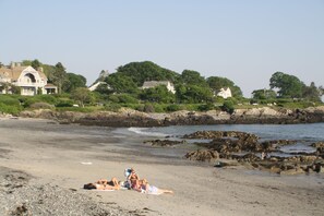 A beach with a few people sunbathing, a rocky shoreline, and houses in the background. - Classic, summer cottage with all the amenities! (Kennebunkport)