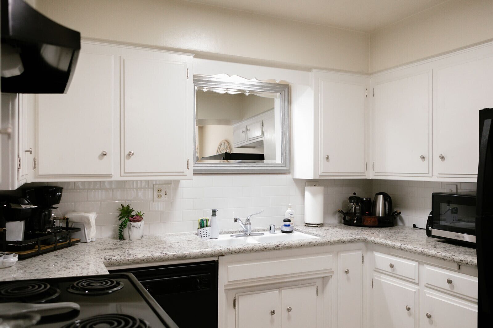 Una cocina moderna con gabinetes blancos, encimera de granito, lavavajillas integrado, estufa, microondas y cafetera.