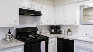 A modern kitchen with white cabinets, a black stove, and a coffee maker.