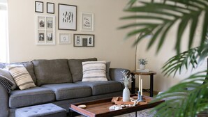 A modern living room with a grey sofa, a wooden coffee table with candles, and framed artwork on the wall.
