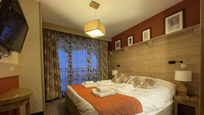 Habitació d'hotel amb llit, televisió, capçalera de fusta, finestra amb cortines i paret vermella.