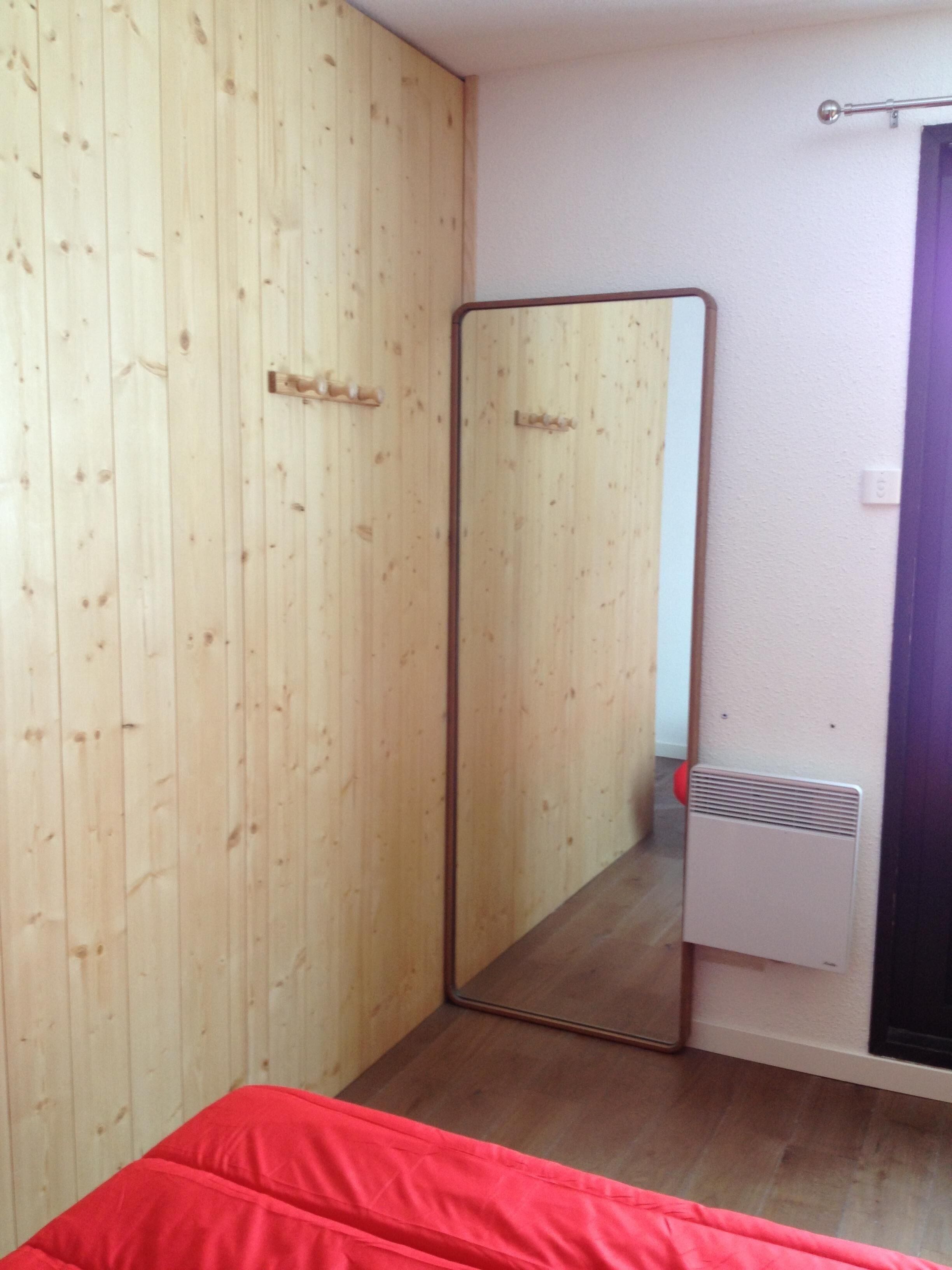 Ein Zimmer mit einem Holzschrank, einem Spiegel, einer Heizung und einem roten Bett.