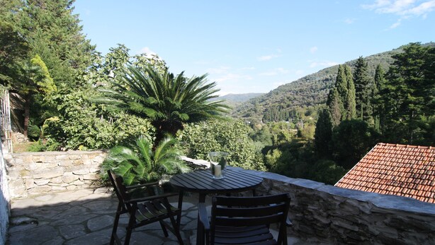 An outdoor patio with stone flooring, two wooden chairs, a round table, and a glass of water. - Centrally located, yet secluded house on the outskirts of Dolcedo (Dolcedo)