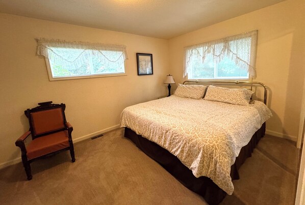 A bedroom with a bed, two windows with lace curtains, a chair, and a bedside lamp. - Cozy step-free house near the downtown waterfront & ferry (Port Orchard)