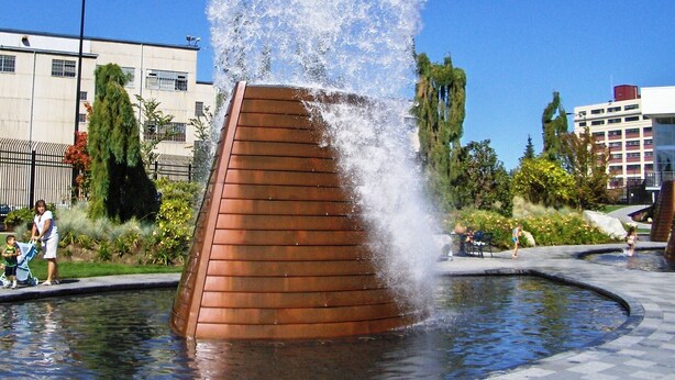Une fontaine d’eau dotée d’une structure en bois, entourée d’une zone pavée et de verdure.