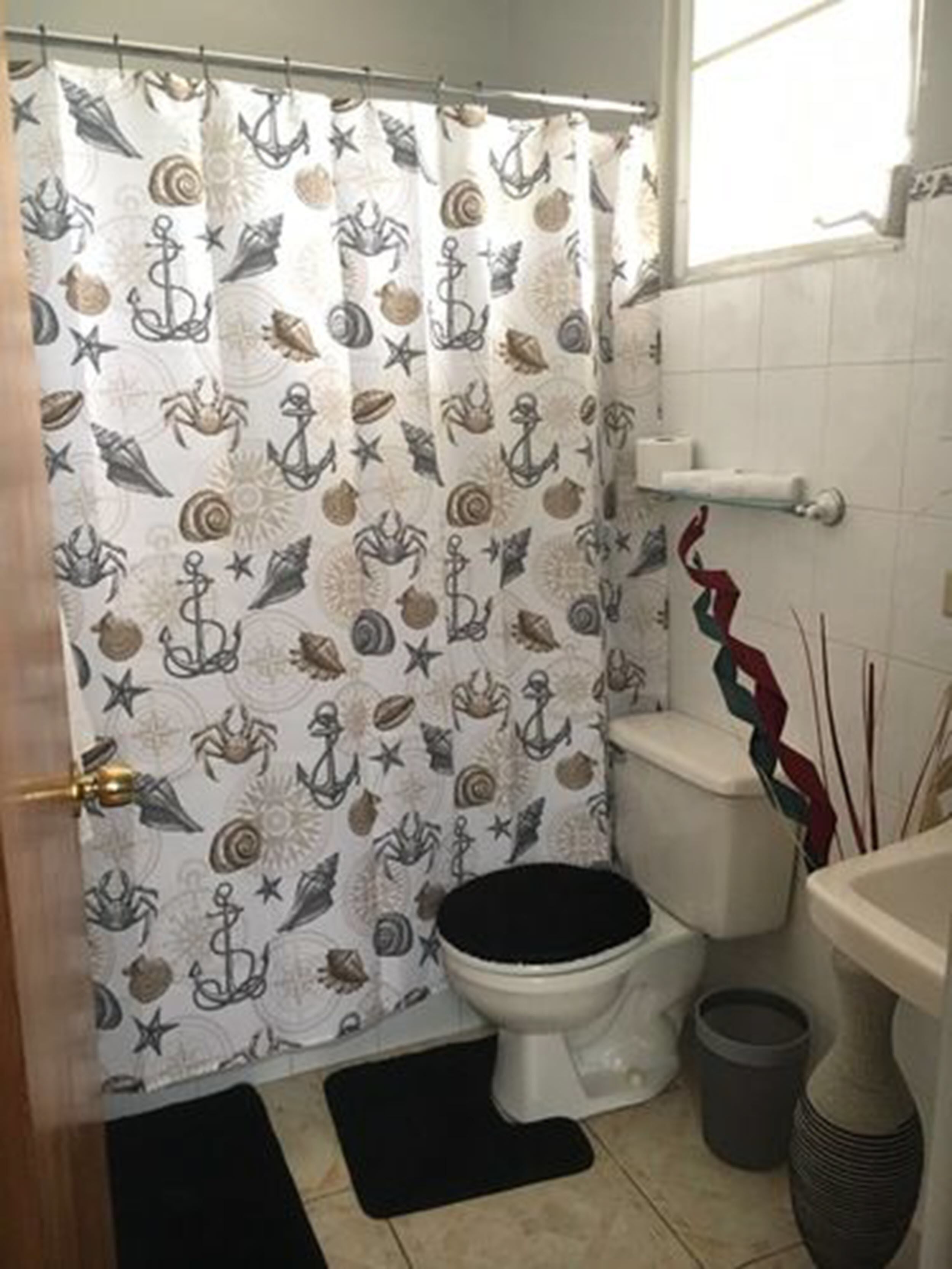 A bathroom with a nautical-themed shower curtain, a toilet, a sink, and a trash can.