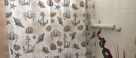 A bathroom with a nautical-themed shower curtain, a toilet, a sink, and a trash can.