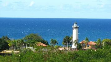 Un phare offrant une vue dégagée sur l’océan, situé dans un cadre tropical avec des palmiers et des bâtiments en arrière-plan.