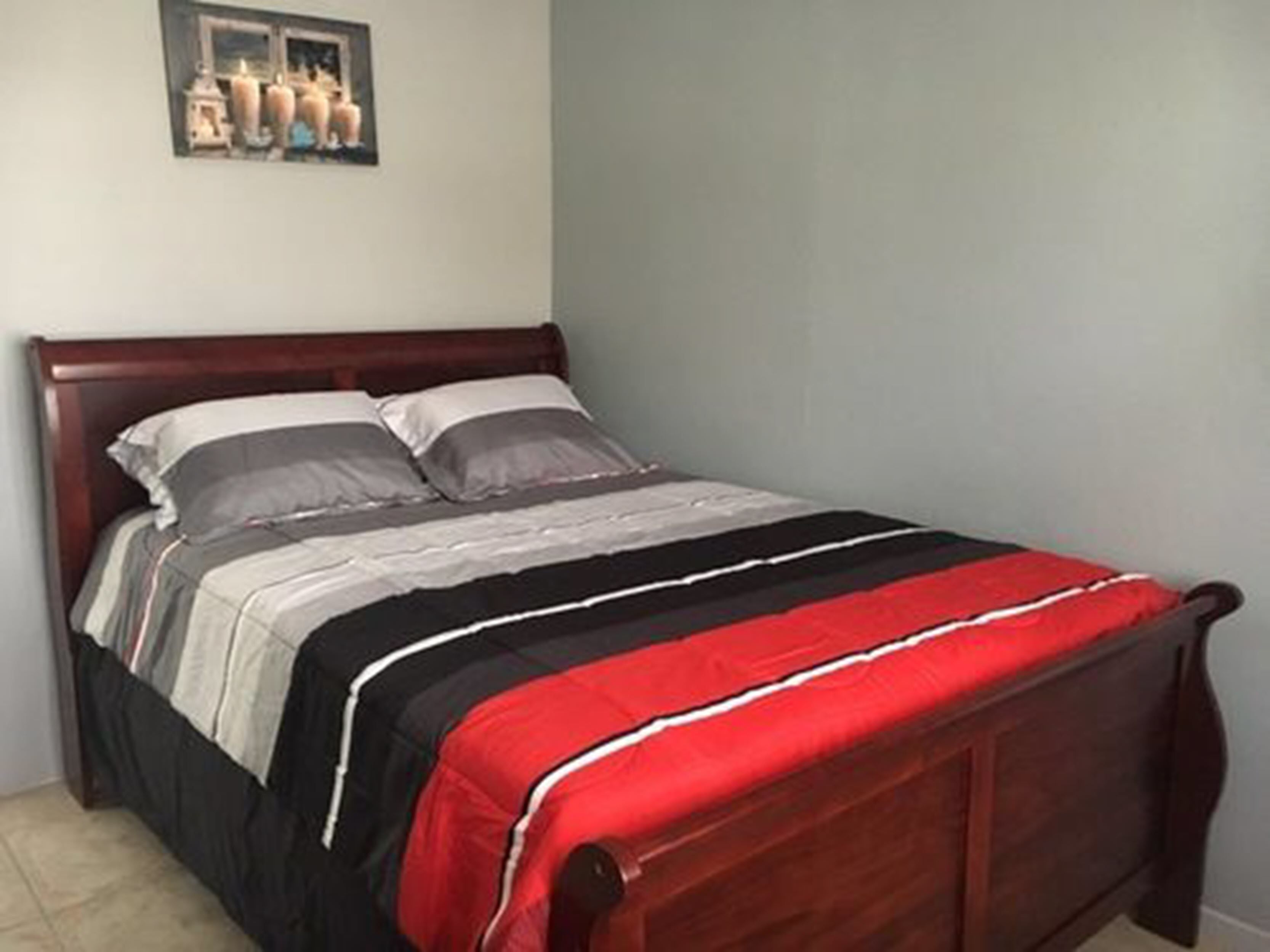 A bed with a wooden headboard, grey and white bedding, and a red blanket.