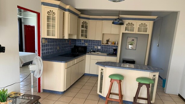 A compact kitchen with a central island, two stools, and a fan. - Boricua Apartments (Rincon)