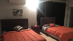 A hotel room with two beds, a nightstand, a wall-mounted air conditioner, and a painting. - Boricua Apartments (Rincon)