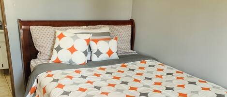 A bed with a geometric patterned bedspread, a wooden headboard, and a wall-mounted picture above the bed.