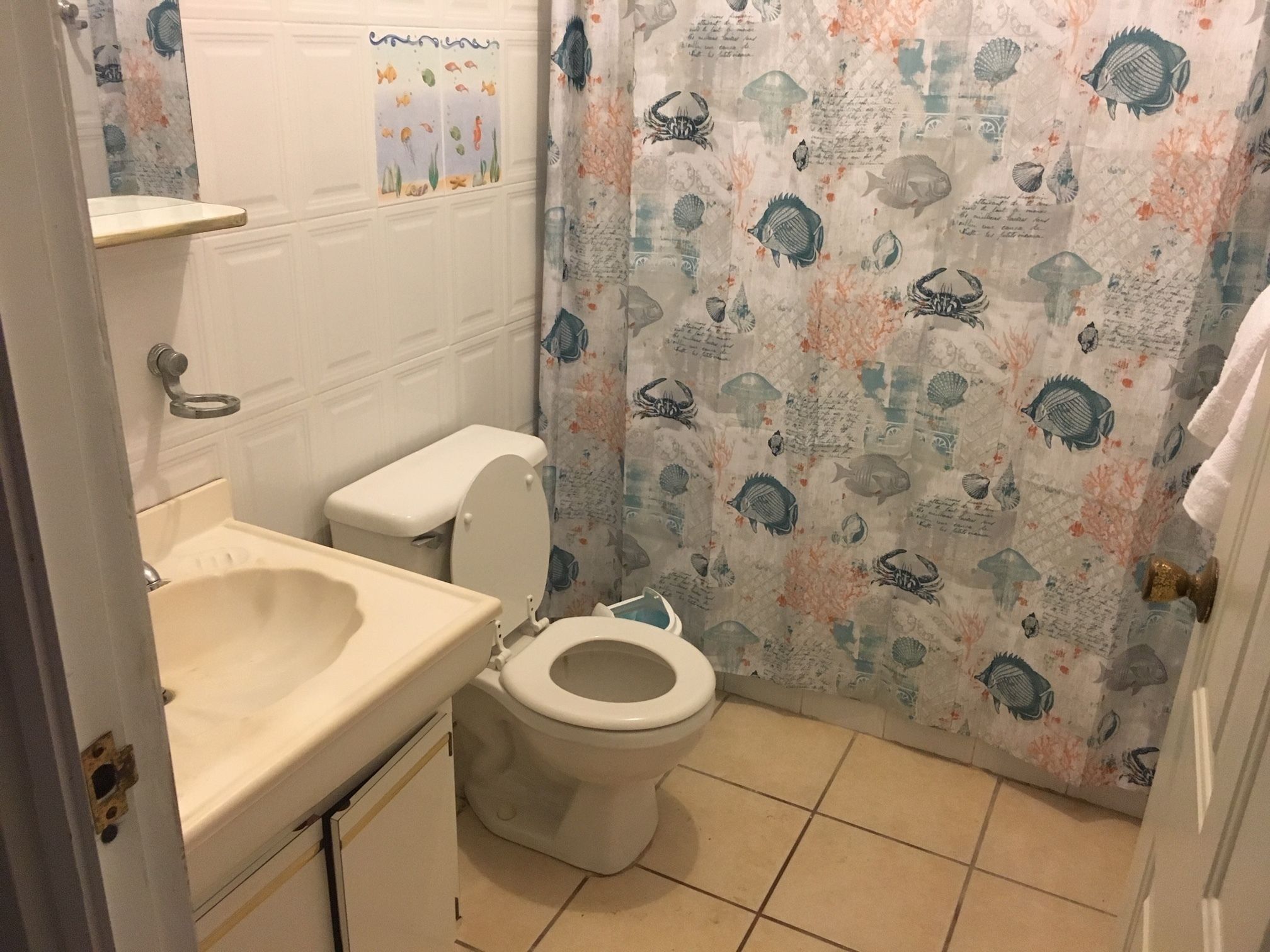 Ein Badezimmer mit Toilette, Waschbecken und einer Duschkabine mit Meeresmotiven.