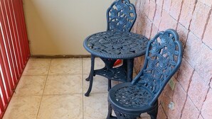 A small balcony with two ornate metal chairs and a table, tiled floor, and a red railing. - Boricua Apartments (Rincon)