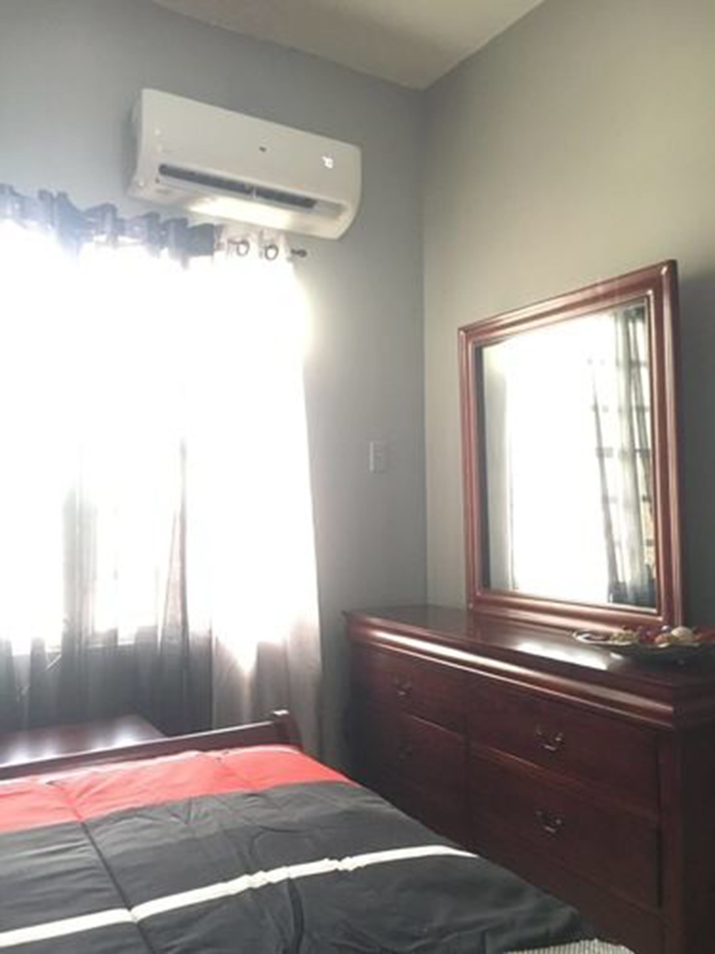 Un dormitorio con cama, cómoda, espejo y equipo de aire acondicionado.