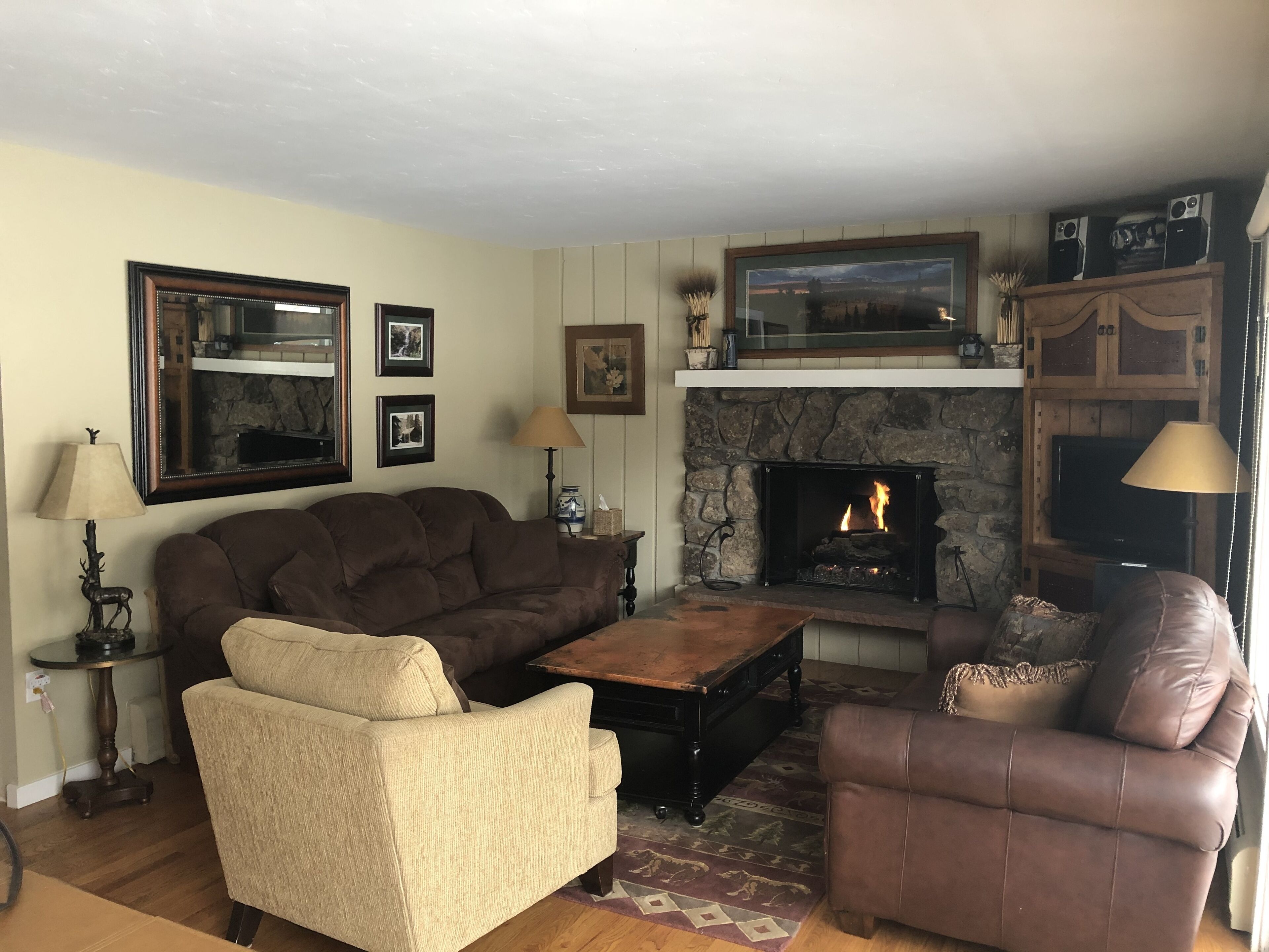 Ein Wohnzimmer mit Kamin aus Stein, zwei Sofas, einem Couchtisch und gerahmten Bildern an der Wand.