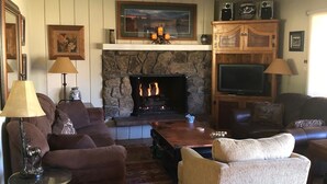 Un salon chaleureux avec une cheminée en pierre, des fauteuils confortables et un téléviseur.