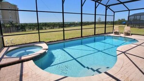 Piscina techada con un jacuzzi, rodeada por una cerca y sillas, con vista a un edificio y árboles al fondo.