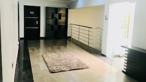 Un pasillo con suelo de baldosas, un tapete, una puerta negra con la letra 'VI' y una escalera con barandilla de metal.