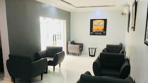 Un área de espera con varios sillones negros, una pequeña mesa redonda y un cuadro en la pared con la imagen de un autobús amarillo.
