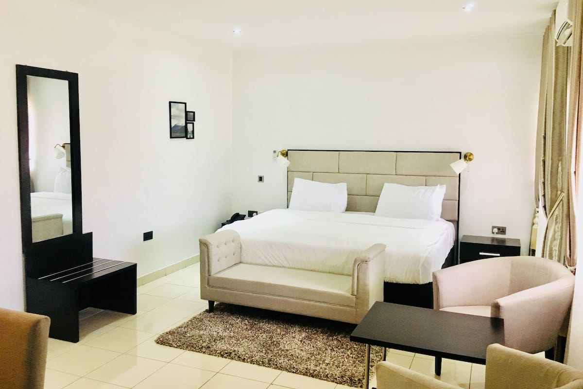 Ein Hotelzimmer mit Bett, Sessel, Tisch, Spiegel und einem kleinen Bild an der Wand.