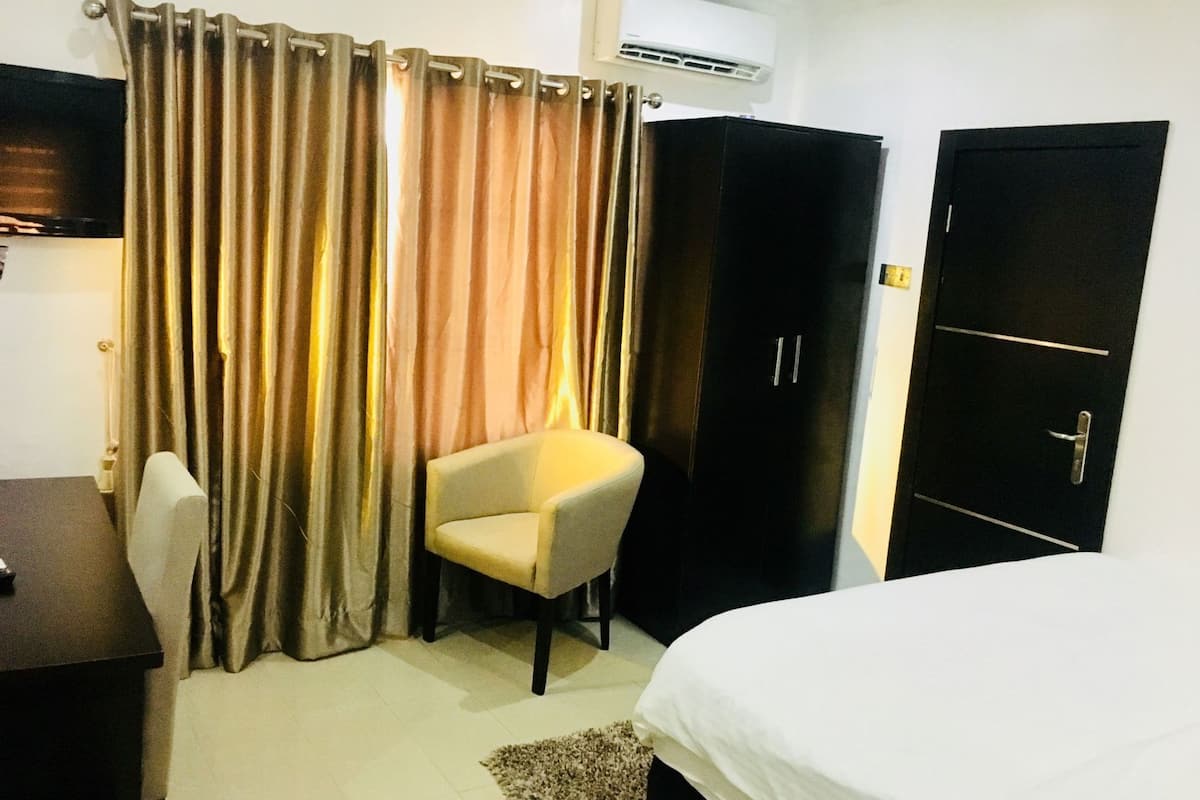 Ein Hotelzimmer mit Bett, Schreibtisch, Stuhl, Kleiderschrank und Vorhängen.