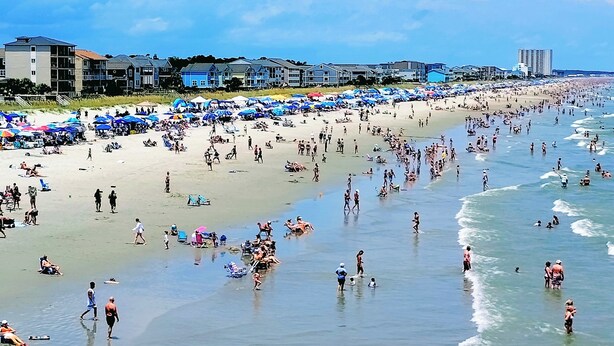 Uma praia cheia de gente caminhando, nadando e tomando sol.
