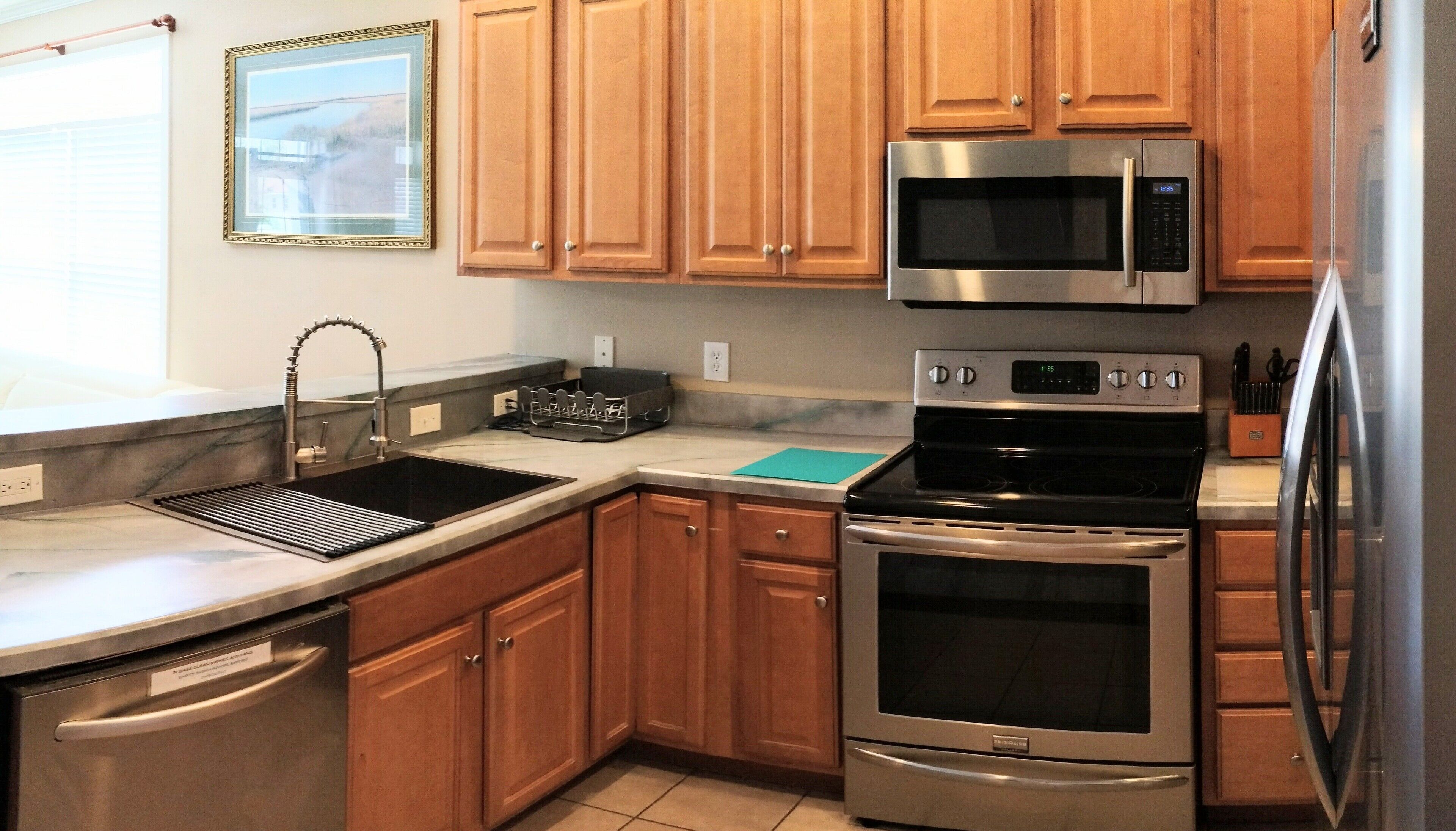 A modern kitchen with wooden cabinets, stainless steel appliances, and a built-in dishwasher.