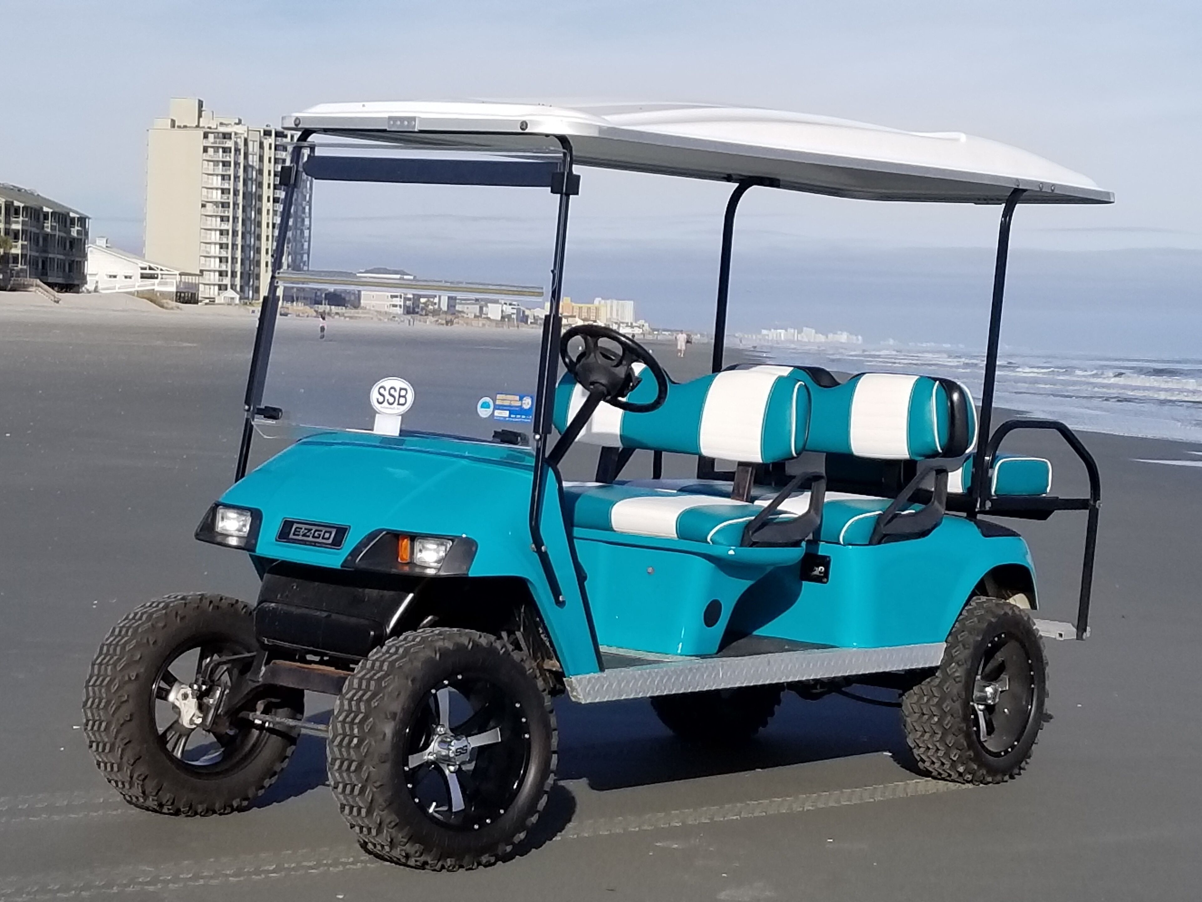 A teal golf cart with a white canopy parked on a sandy beach.
