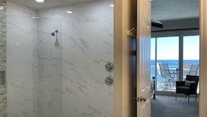 A modern bathroom with a glass-enclosed shower and marble walls.