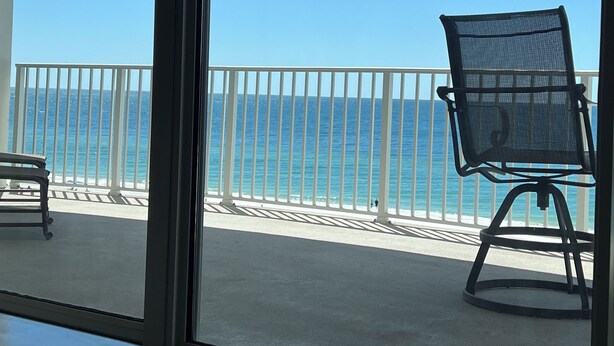 A balcony with a view of the ocean, a chair, and a table.