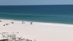 A beach with white sand and a clear blue ocean. There are several umbrellas and beach chairs.