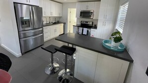 A modern kitchen with stainless steel appliances, white cabinetry, and a bar area with stools.