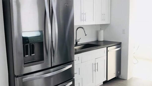 A modern kitchen with stainless steel appliances, white cabinetry, and a black countertop.