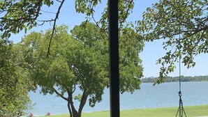 A hammock swing hanging from a tree, a grassy area, and a body of water in the background.