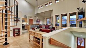 A spacious living area with a wooden staircase, a dining table, and a red sofa.
