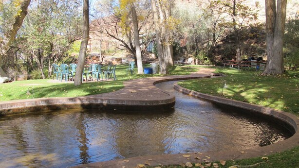 A park with a curved water feature, picnic tables, and green chairs.